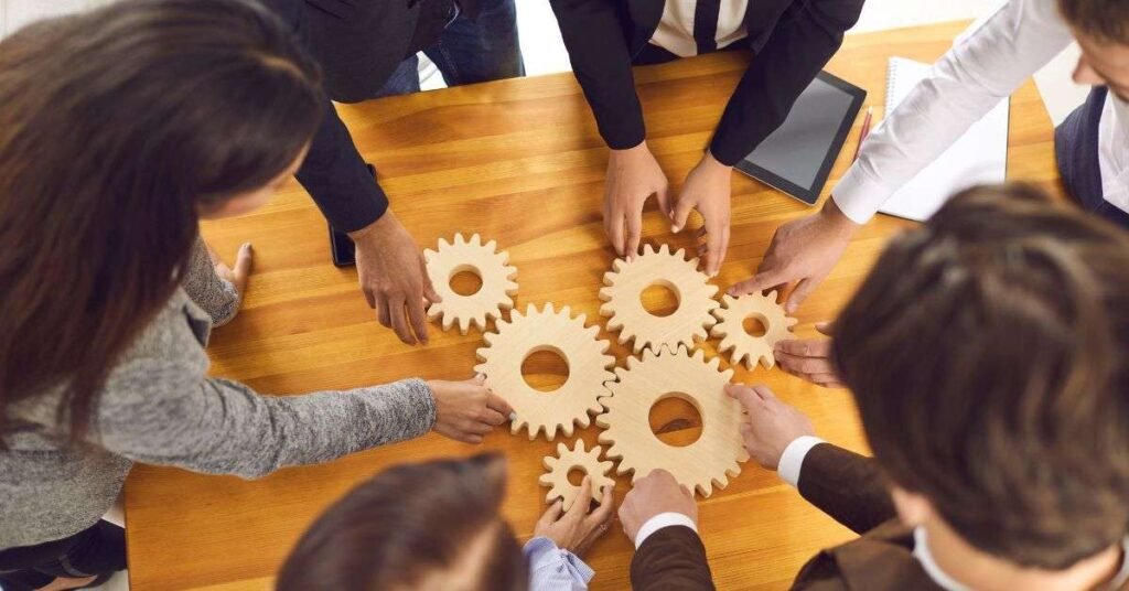 Group of people arranging wooden gear pieces together on a table, symbolizing teamwork and collaboration.