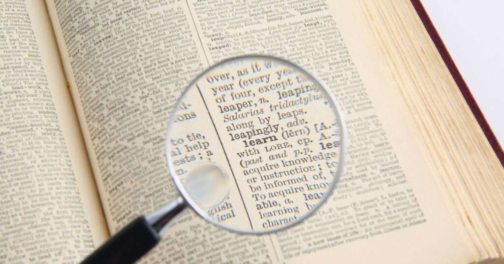 A magnifying glass focusing on printed dictionary text, symbolizing searching and learning information.