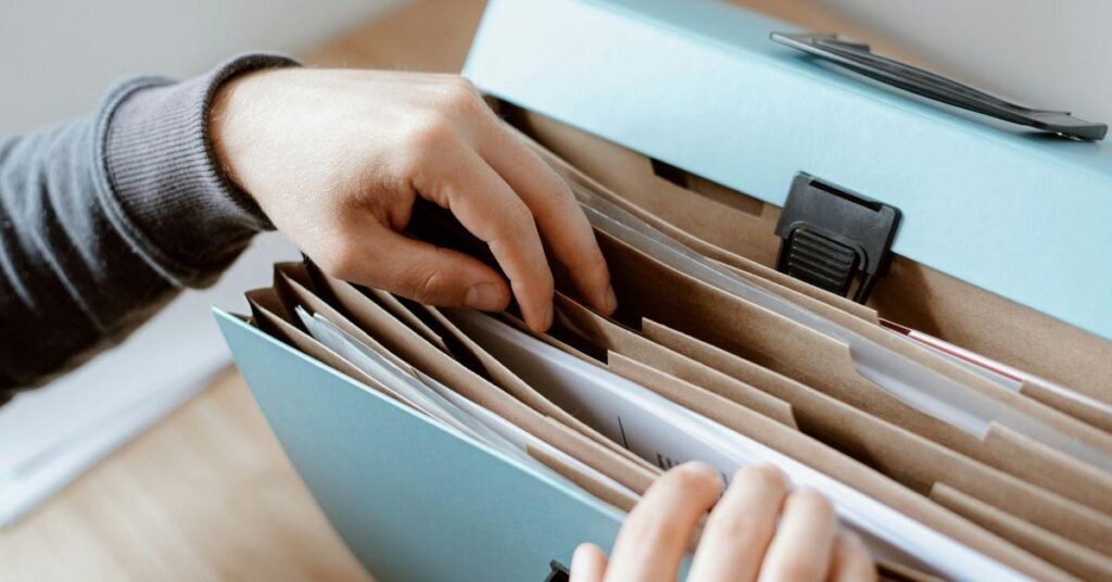 Hands organizing documents in a file cabinet, sorting folders for office paperwork and records storage archive